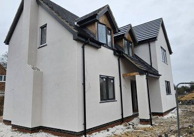 Newly constructed white-rendered house with black roof tiles and a chimney