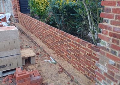 Partially built red brick garden wall with stacked bricks and construction materials
