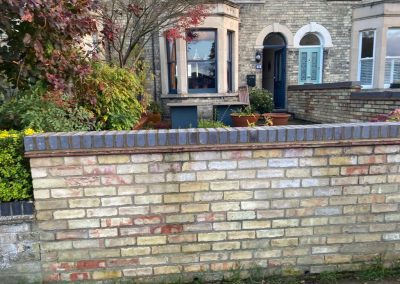 Front garden brick wall with dark coping bricks, set against a Victorian-style house and lush garden