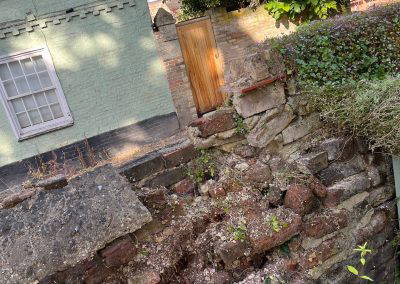 A weathered and partially deteriorated brick wall with overgrown vegetation